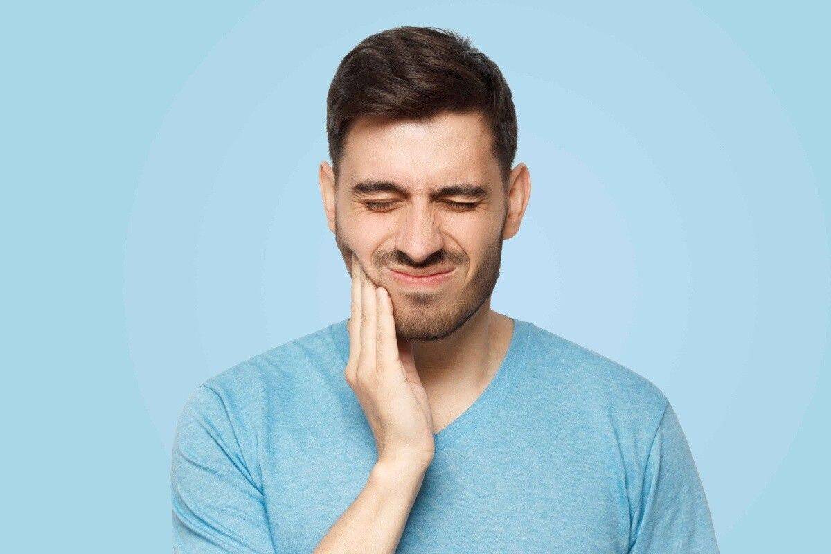 Man holding cheek due to severe tooth pain requiring emergency dental care