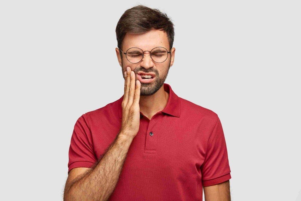 Man holding his cheek due to severe tooth pain before an emergency dental visit