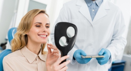 A Lady smiling looking at her teeth in the mirror beside her dentist
