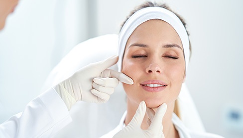 A dentist gently touching the face and mouth of her female patient who is closing her eyes