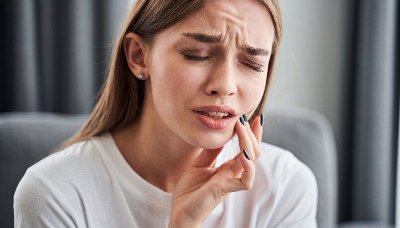 A woman holding her cheek and wincing in pain enduring a toothache